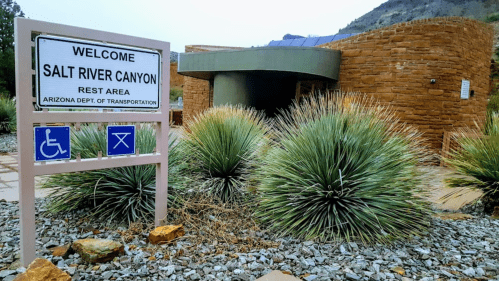 Sign for Salt River Canyon Rest Area, featuring a stone building and desert vegetation in a scenic landscape.